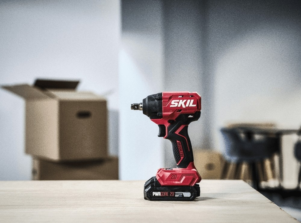 Un avvitatore a impatto SKIL rosso e nero si trova su un tavolo di legno con sfondo sfocato.