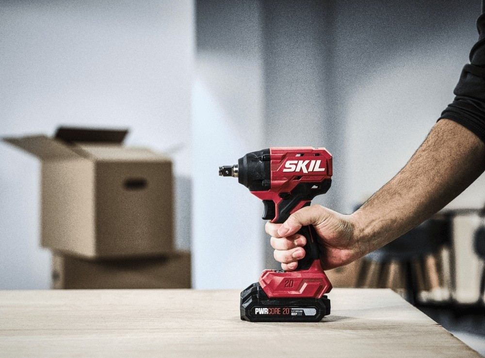 Mano tiene un avvitatore a impatto cordless SKIL rosso su una superficie di legno.