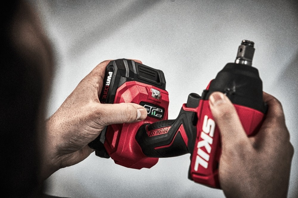 Una persona tiene in mano un avvitatore a impatto cordless Skil rosso e nero.