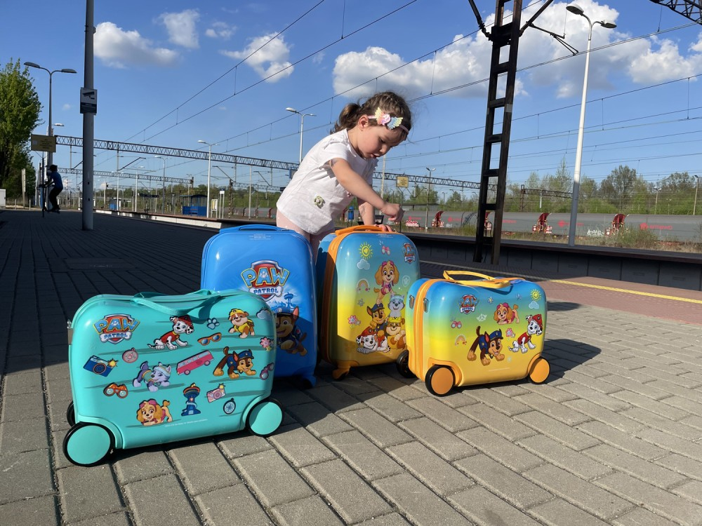 Dziewczynka stoi na peronie kolejowym z czterema kolorowymi walizkami Psi Patrol.