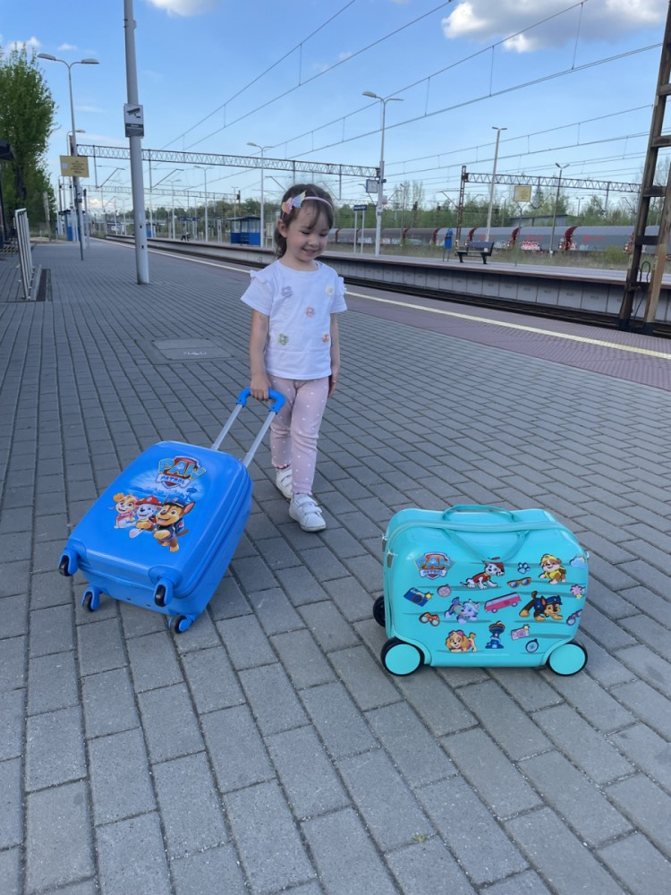 Mała dziewczynka z dwoma walizkami Paw Patrol stoi na peronie.