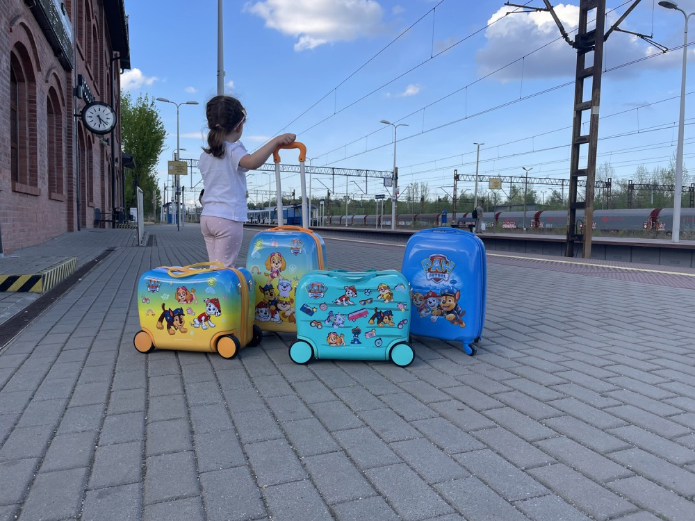 Mała dziewczynka stoi na perone stacji kolejowej z czterema kolorowymi walizkami Psi Patrol.