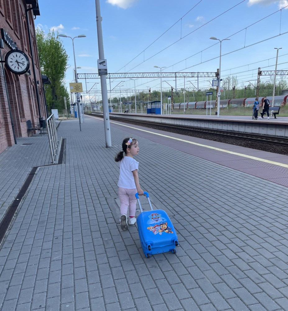 Małe dziecko ciągnie niebieską walizk ę po peronie stacji kolejowej.
