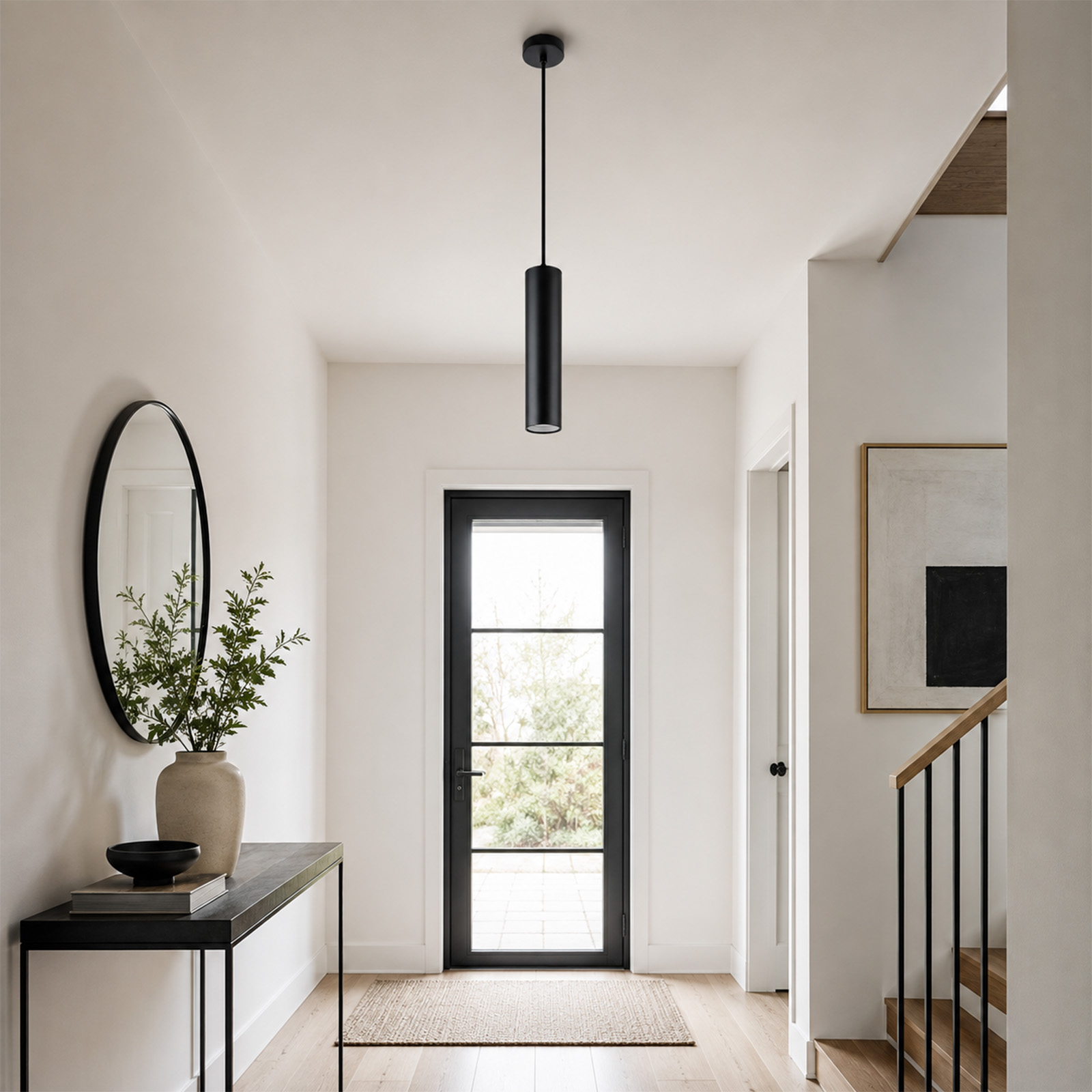 Pasillo luminoso con paredes blancas, lámpara colgante negra, puerta de cristal, consola, espejo y escaleras.