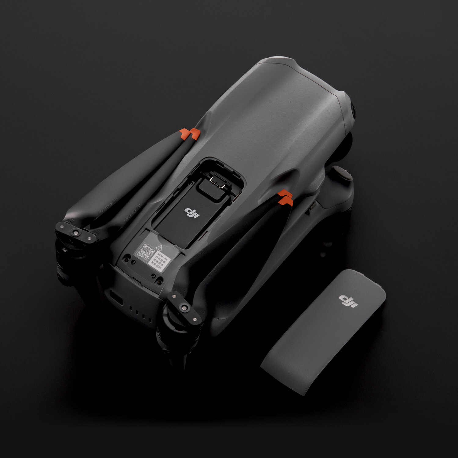 Un drone DJI grigio con bracci piegati su sfondo nero e la sua batteria accanto.