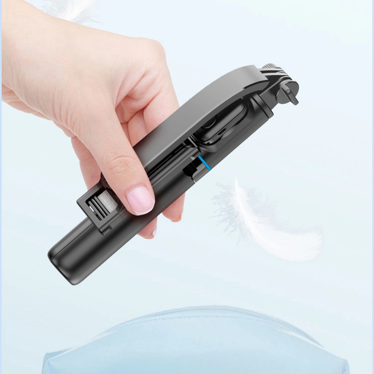 Una mano tiene un selfie stick compatto nero su sfondo azzurro.