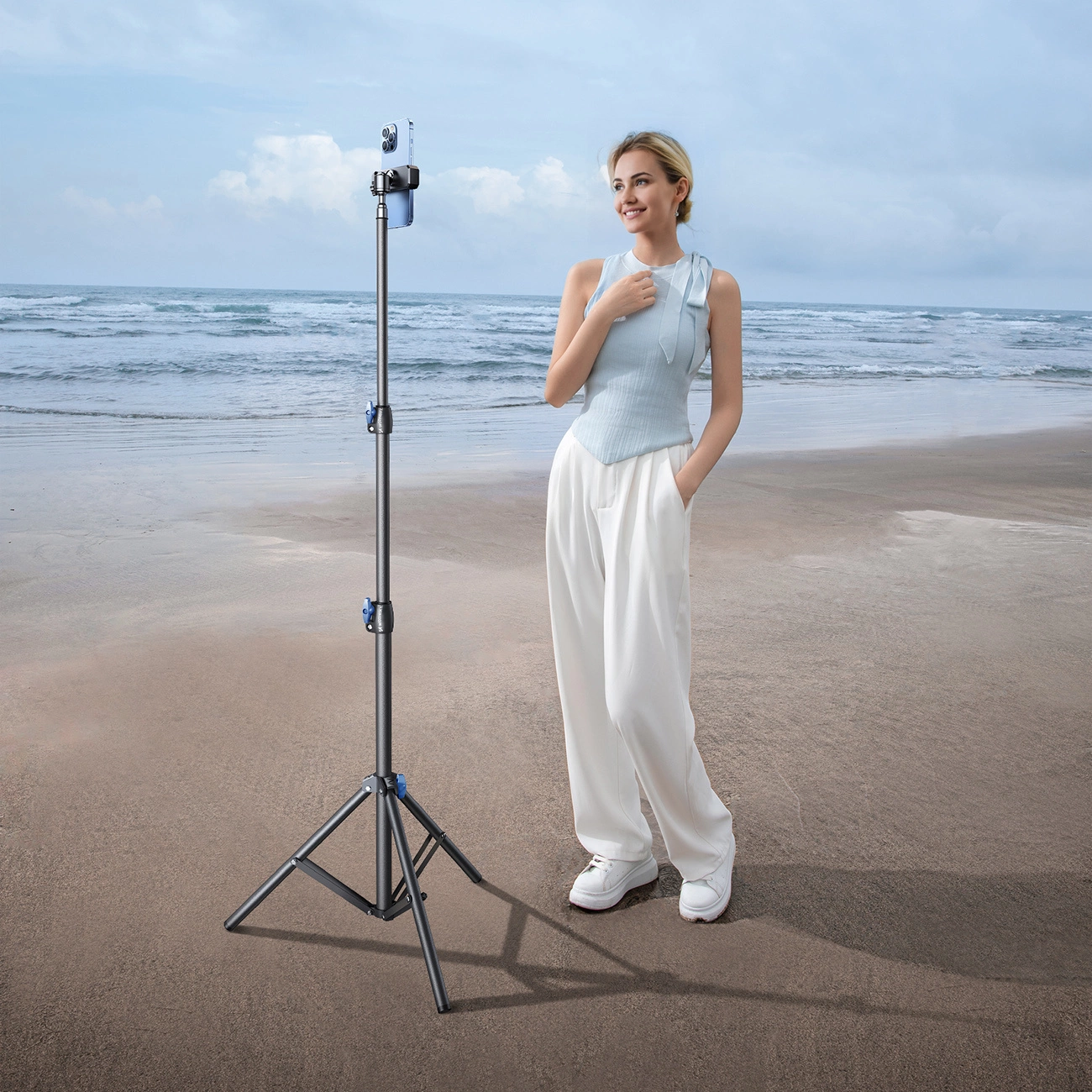 Una donna è sulla spiaggia accanto a un treppiede con smartphone.