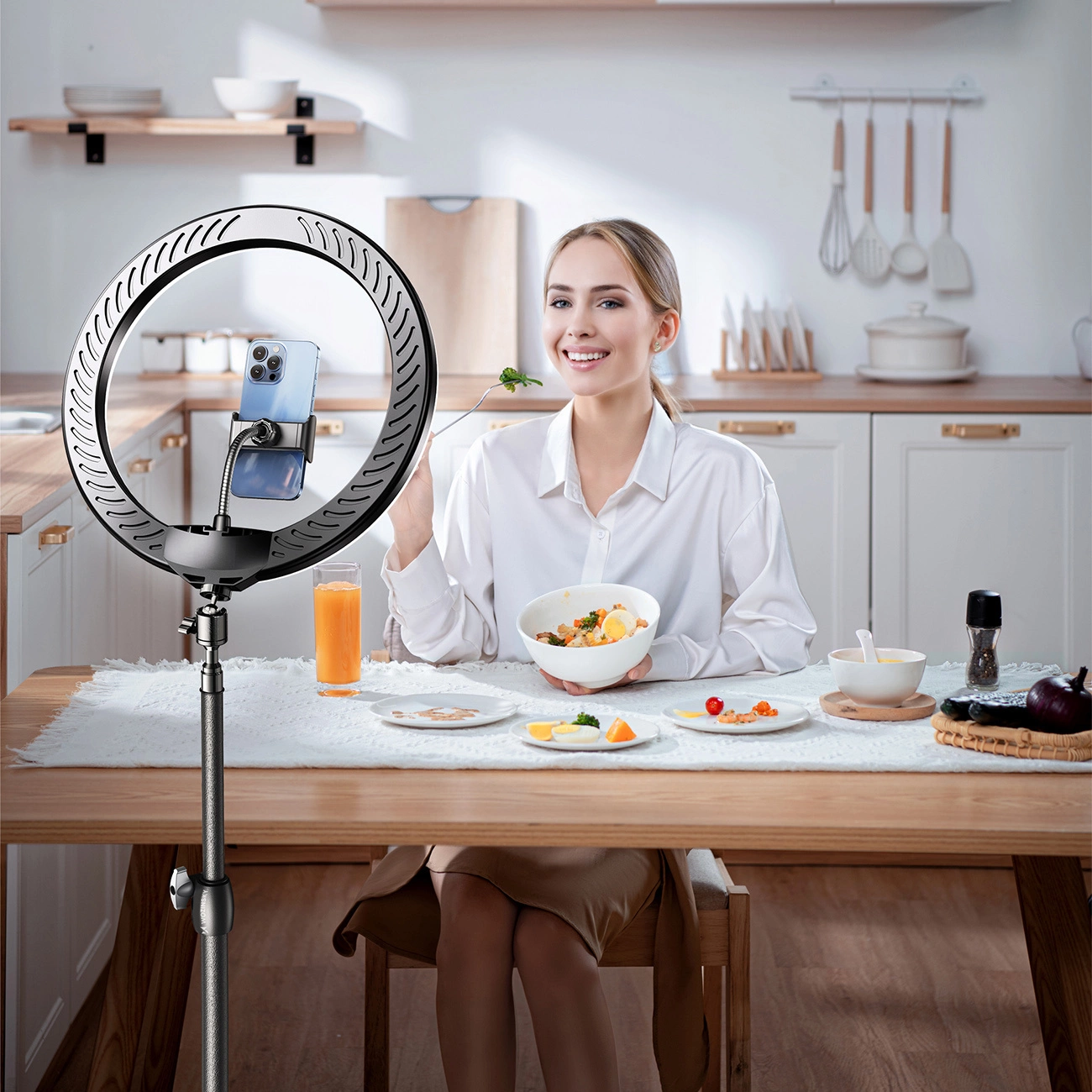 Una donna siede al tavolo della cucina tenendo una ciotola mentre uno smartphone su una ring light la riprende.