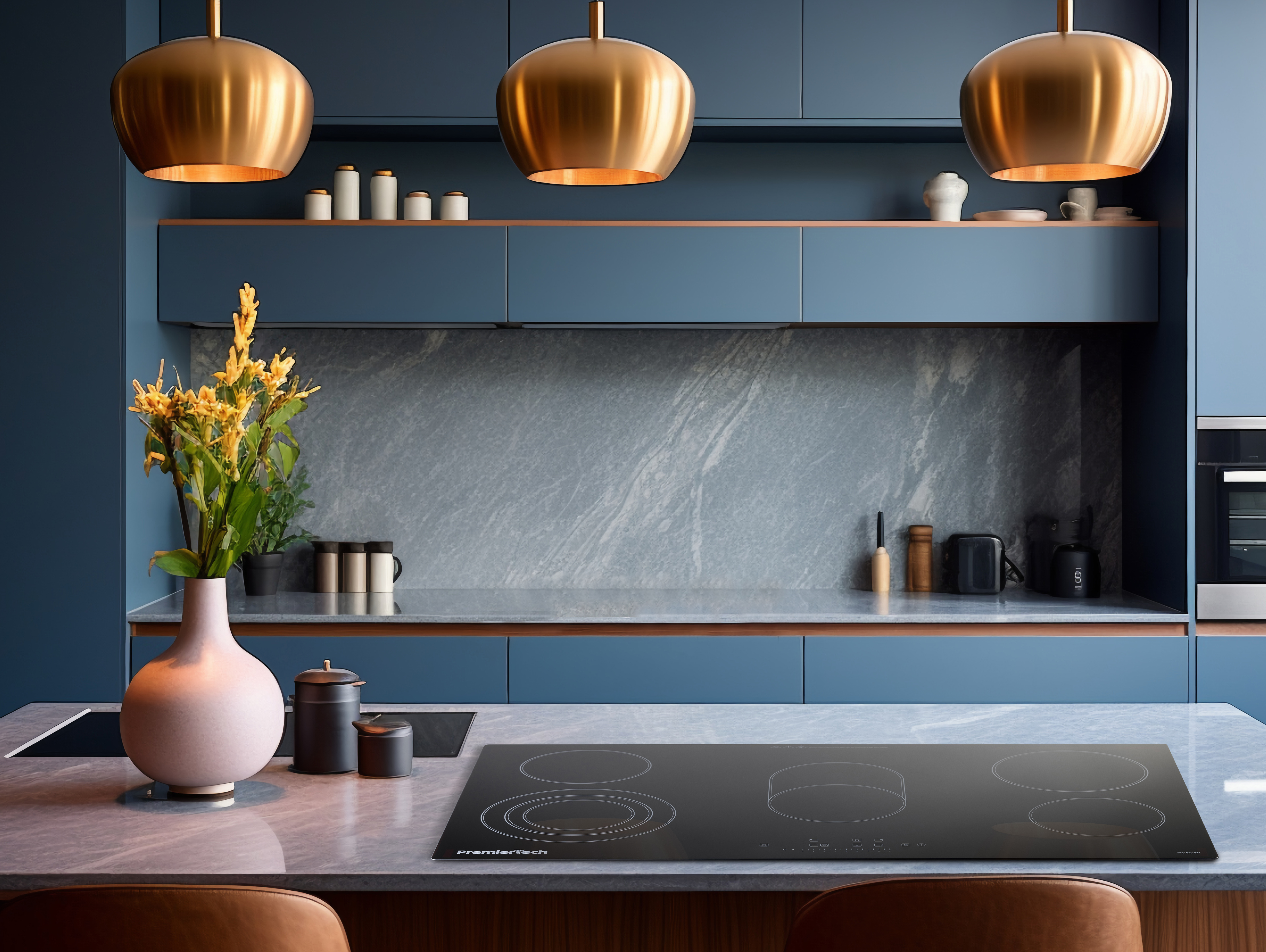 Moderna cucina blu con piani in marmo, lampade a sospensione dorate, vaso rosa con fiori gialli e piano cottura.