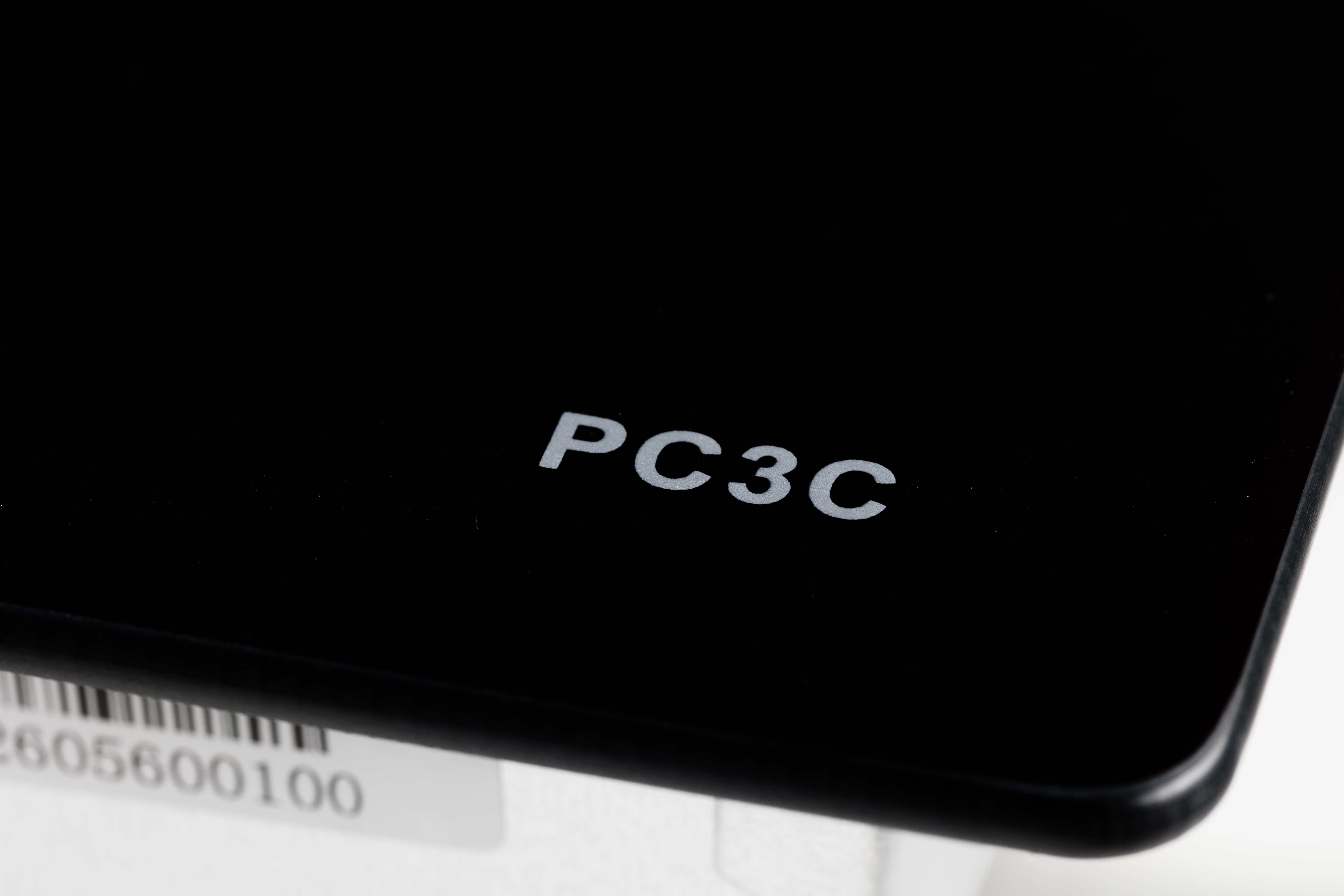 Primo piano della scritta PC3C su superficie nera lucida con parte di codice a barre.