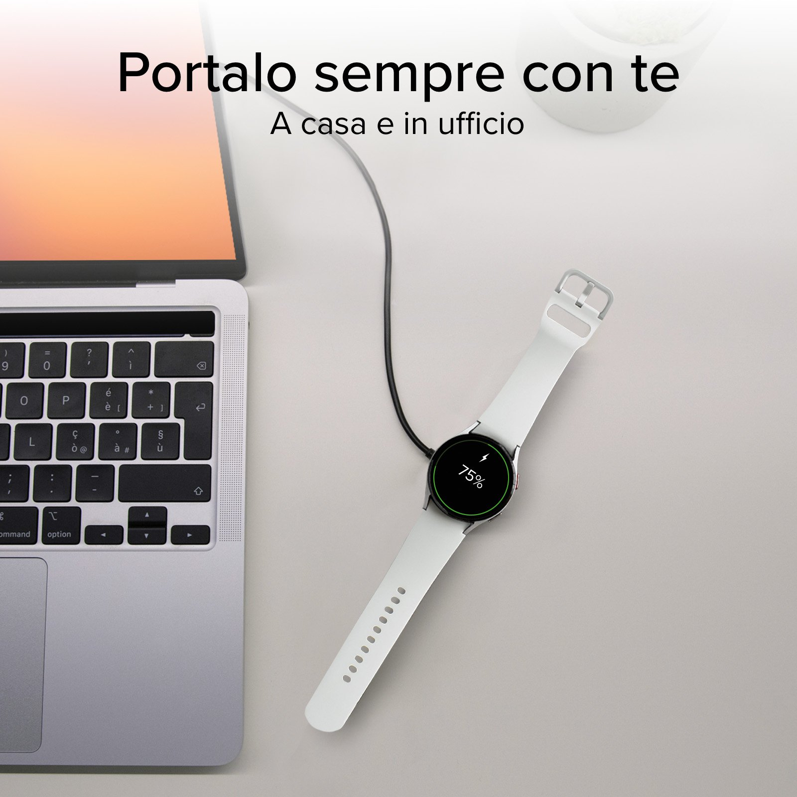 Uno smartwatch con cinturino bianco poggia su un tavolo, in carica con un cavo accanto a un computer portatile.