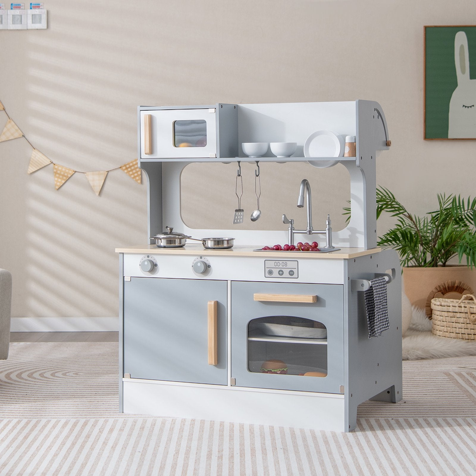 Une cuisine jouet en bois gris et blanc se trouve sur un tapis dans une pièce.