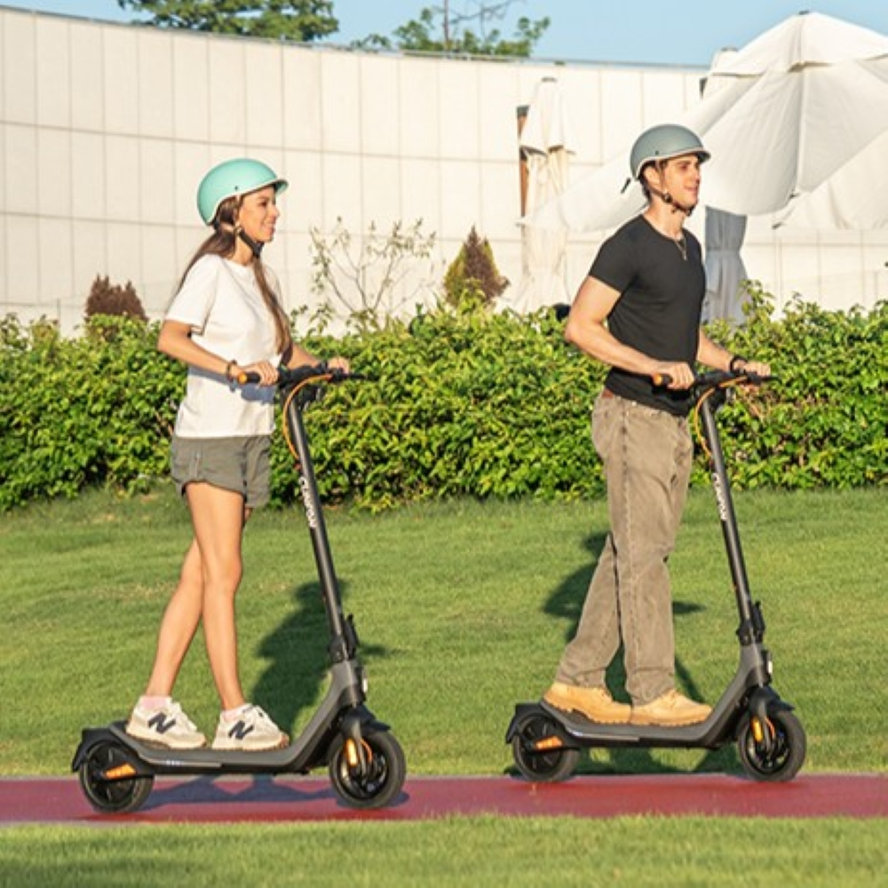 Due persone con il casco guidano monopattini elettrici su un percorso rosso all'aperto.