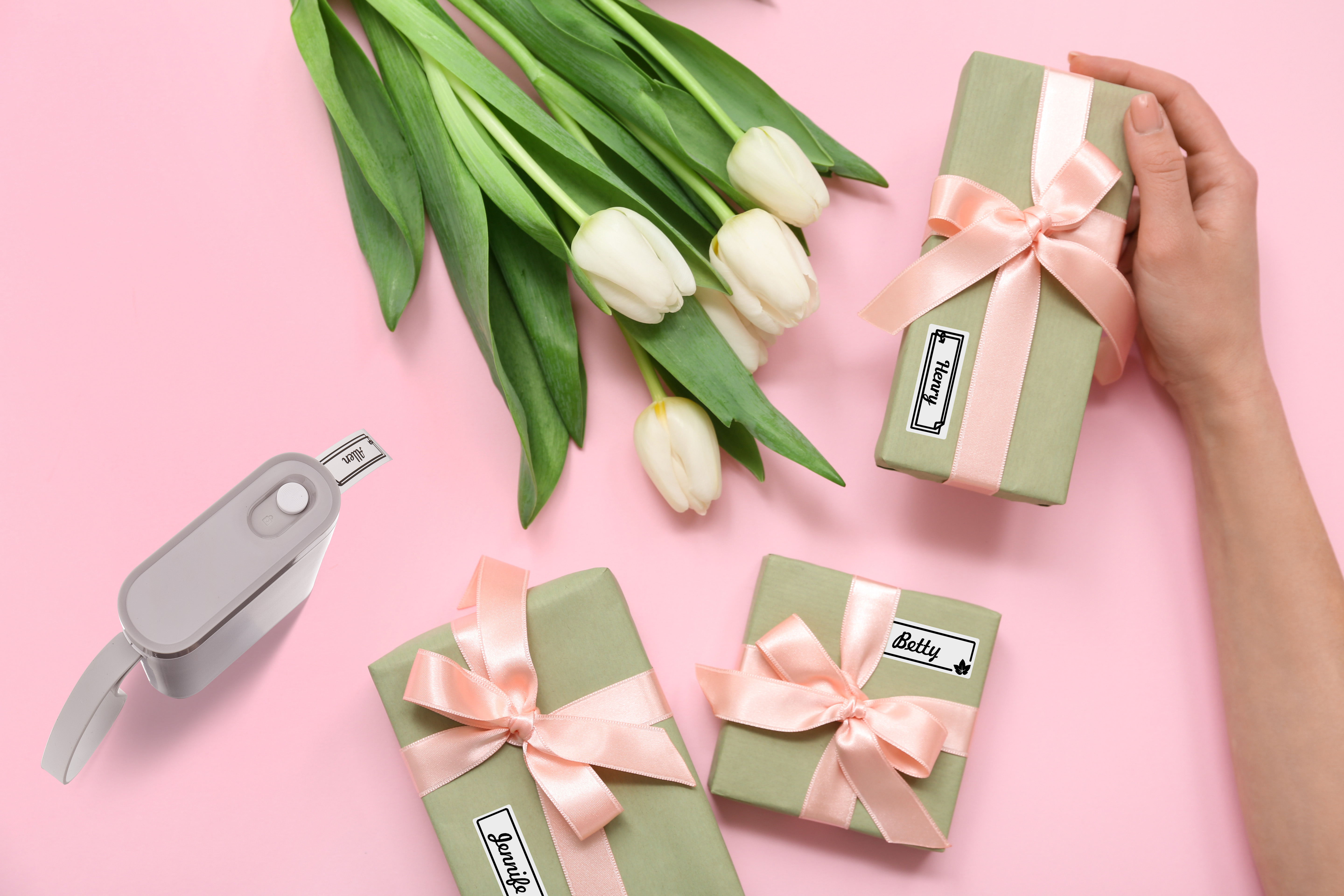 Cadeaux verts avec rubans roses, tulipes blanches et étiqueteuse sur fond rose.