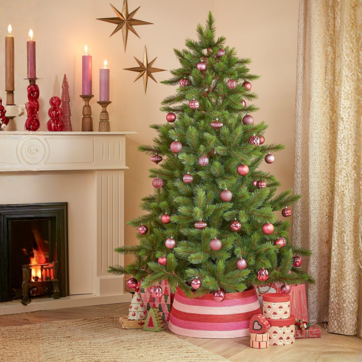Un sapin de Noël aux boules roses près d'une cheminée avec des bougies.