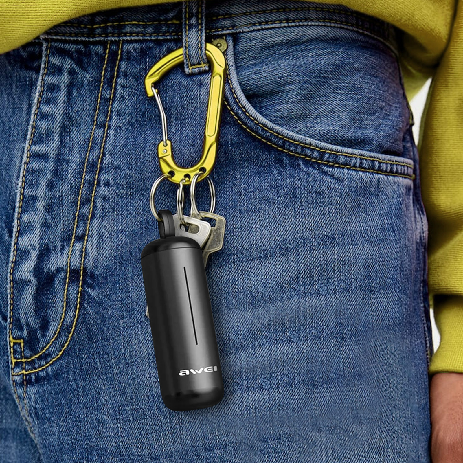 Un oggetto nero a forma di capsula e delle chiavi appendono a un moschettone giallo sui jeans blu.