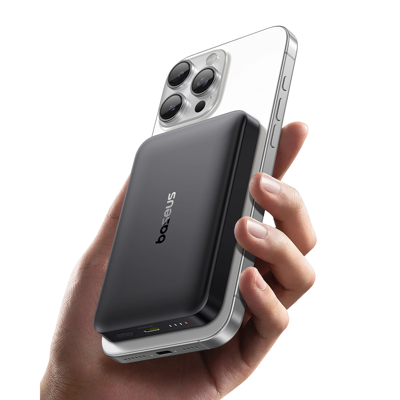 Una mano tiene uno smartphone argento con un power bank nero Baseus sul retro su sfondo bianco.
