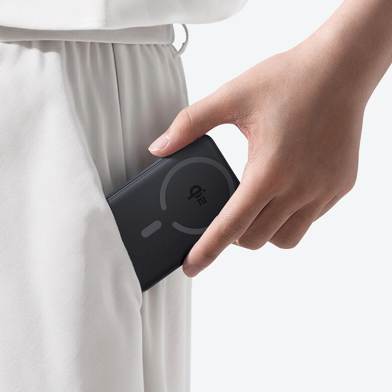 Una mano ripone un power bank nero nella tasca dei pantaloni bianchi.