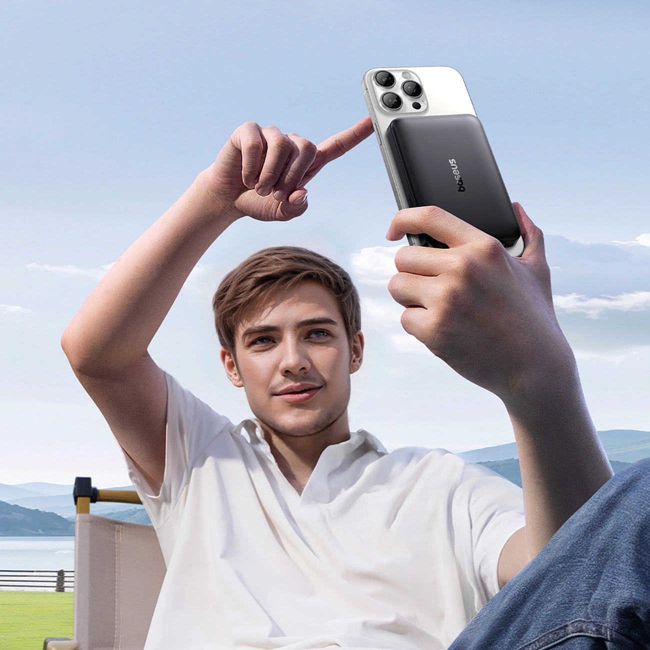 Un giovane con camicia bianca siede all'aperto e indica uno smartphone con power bank.