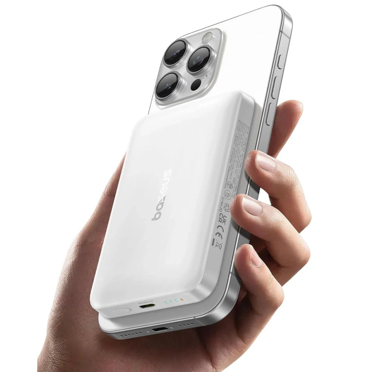 Una mano tiene uno smartphone argento con una power bank bianca.