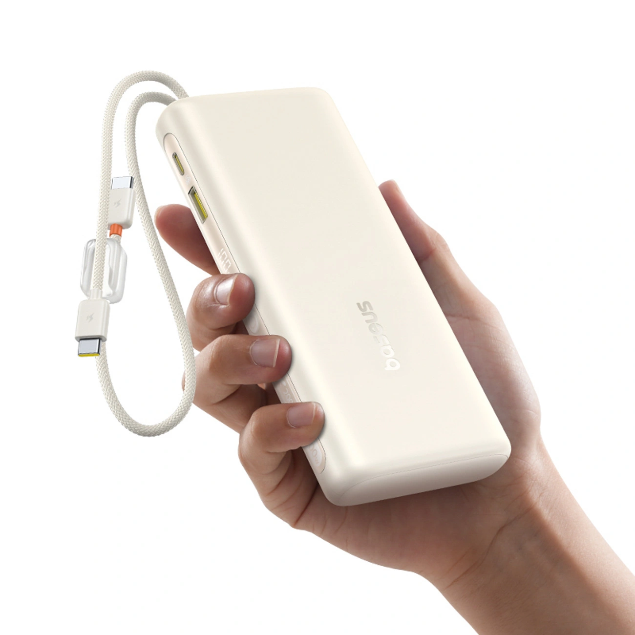 Una mano tiene un power bank Baseus beige con cavo di ricarica integrato su sfondo bianco.