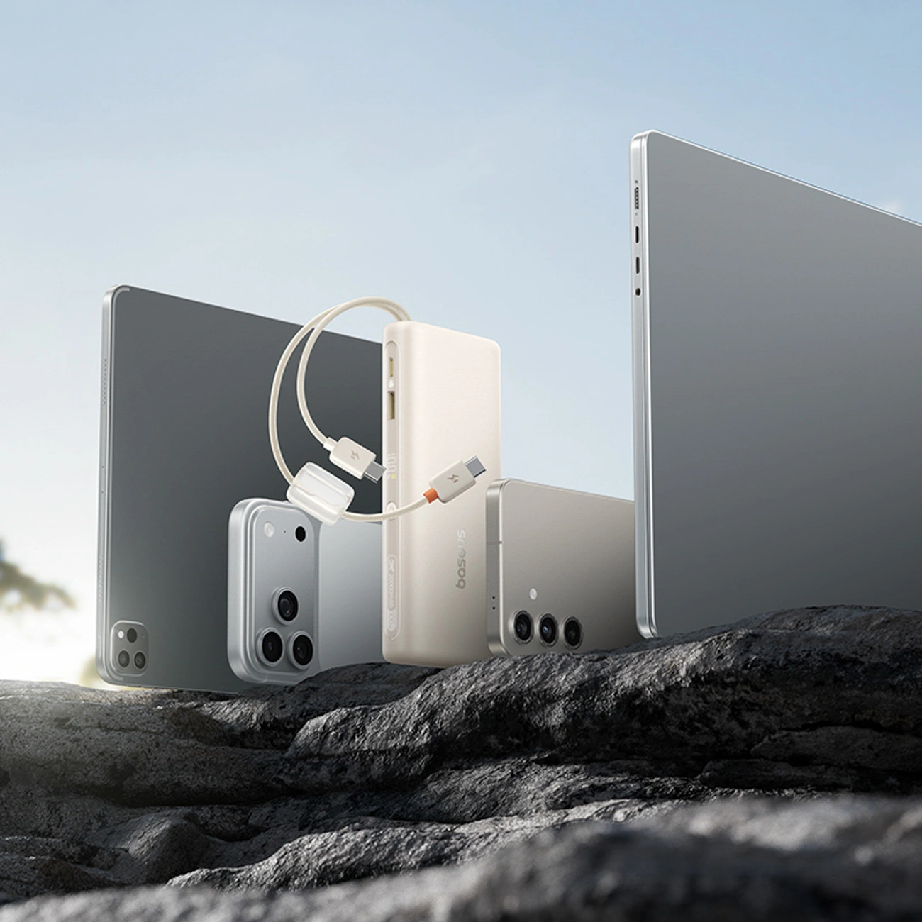Dispositivi elettronici moderni, tablet e smartphone con power bank su una superficie rocciosa.