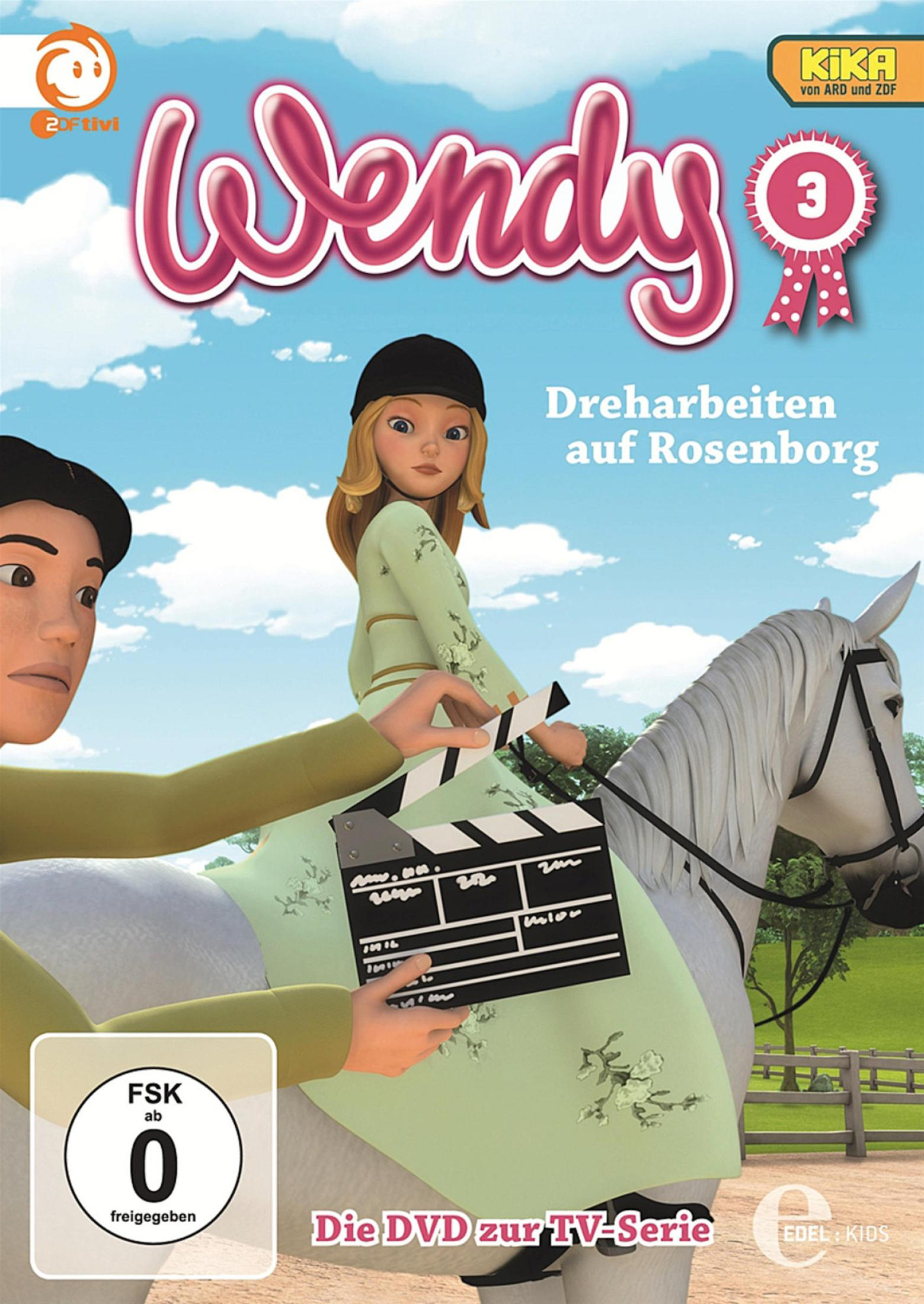 Wendy reitet auf einem weißen Pferd, während jemand eine Filmklappe hält; im Hintergrund ein blauer Himmel mit Wolken.