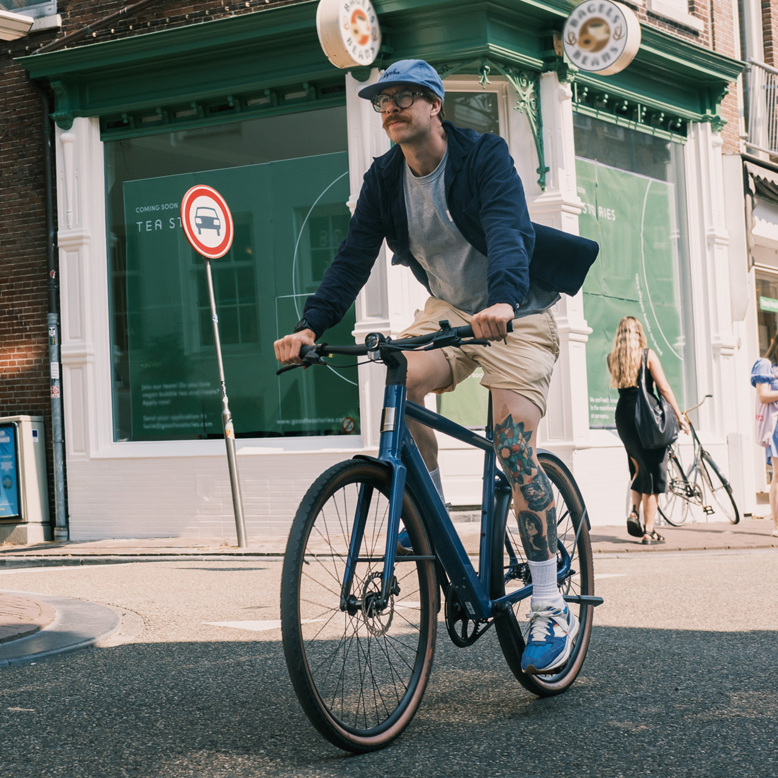 Ein Mann mit blauer Kappe fährt ein blaues Fahrrad vor einer grünen Ladenfront.