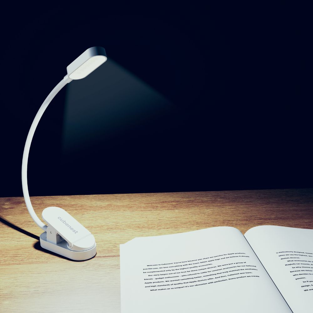 Eine weiße Clip-Schreibtischlampe beleuchtet ein aufgeschlagenes Buch auf einem Holztisch vor schwarzem Hintergrund.