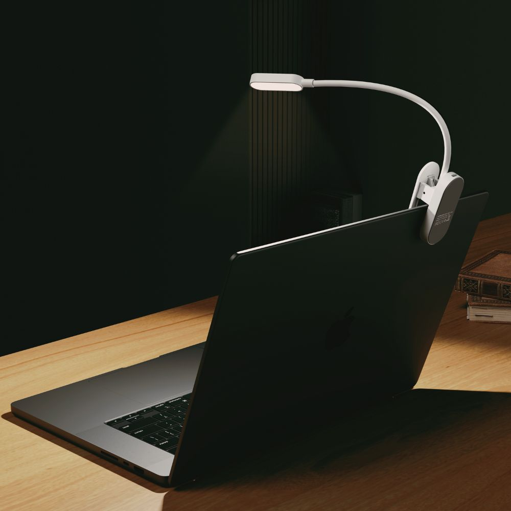 Eine weiße Clip-LED-Leselampe an einem Laptop-Bildschirm auf einem Holztisch.