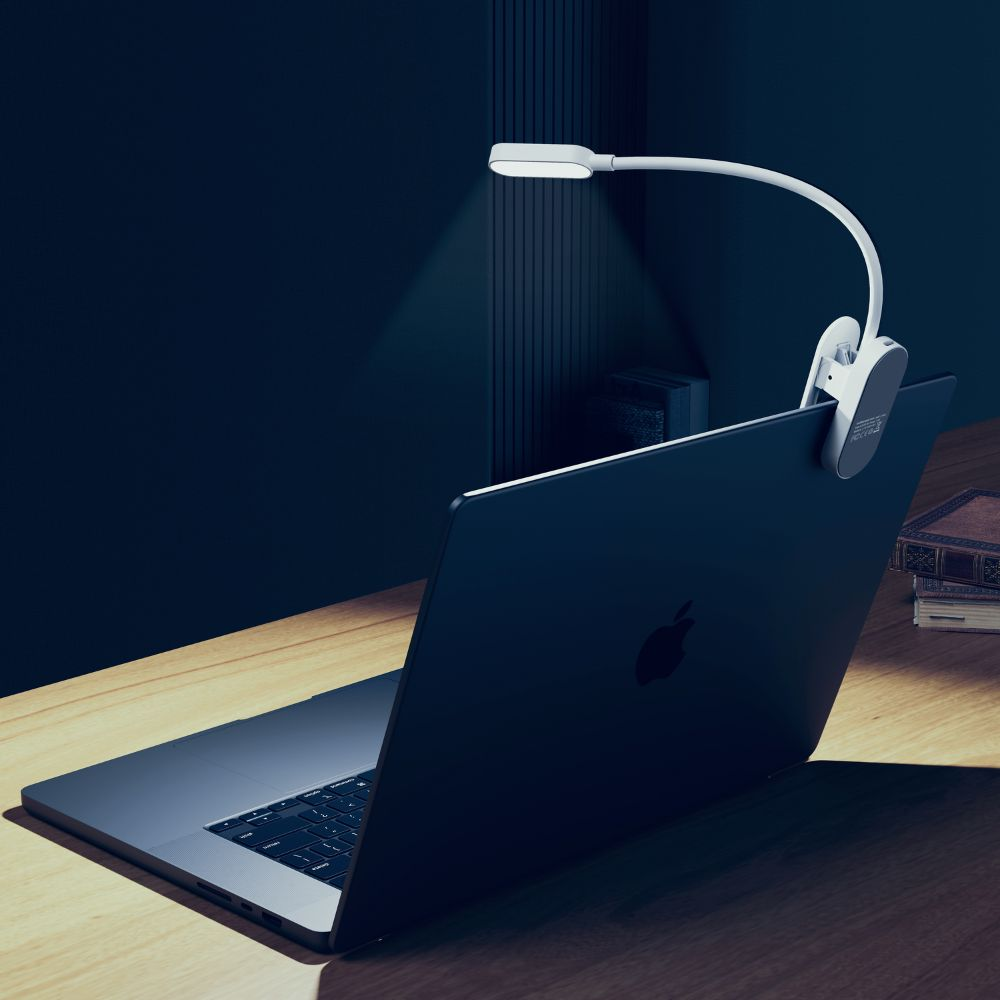 Eine weiße Klemmlampe ist am Bildschirm eines MacBooks auf einem Schreibtisch befestigt und beleuchtet ihn.