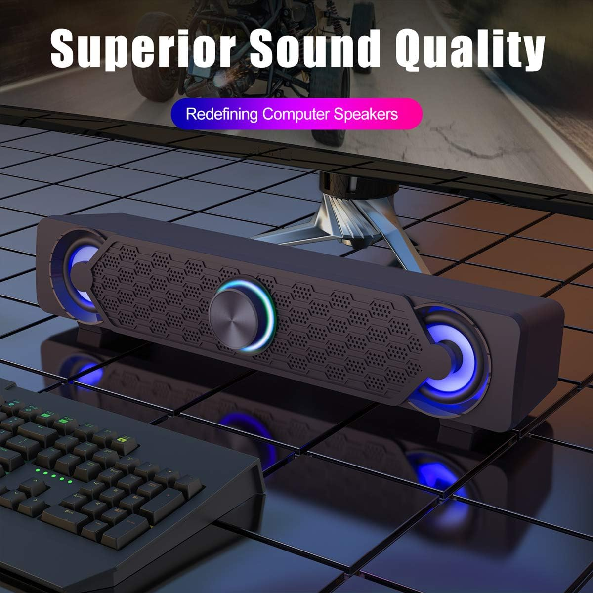Eine schwarze Computer-Soundbar mit blauer Beleuchtung steht auf einem reflektierenden Tisch neben einer Tastatur.