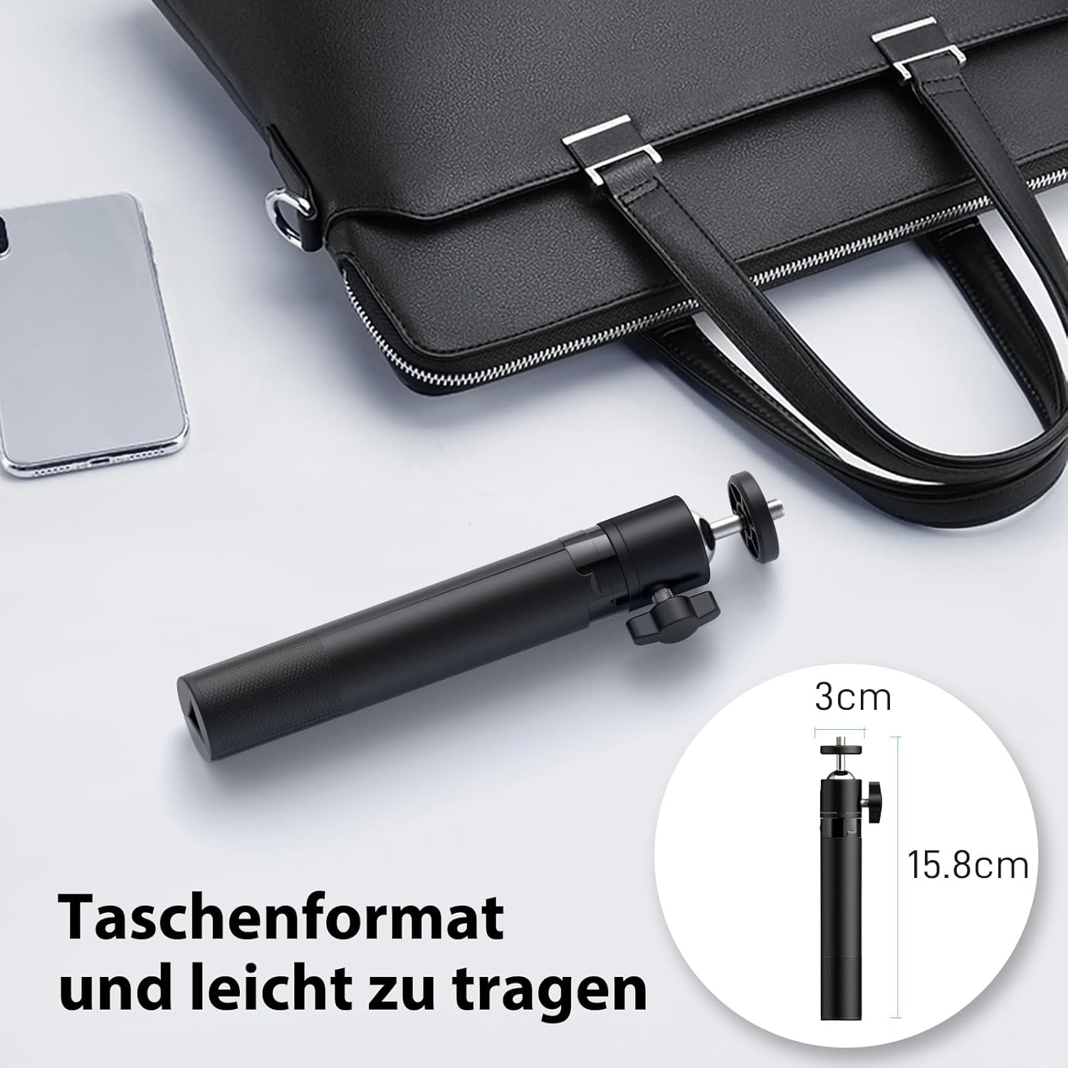 Ein schwarzes Mini-Stativ liegt neben einer Handtasche und einem Smartphone, mit Maßangaben.