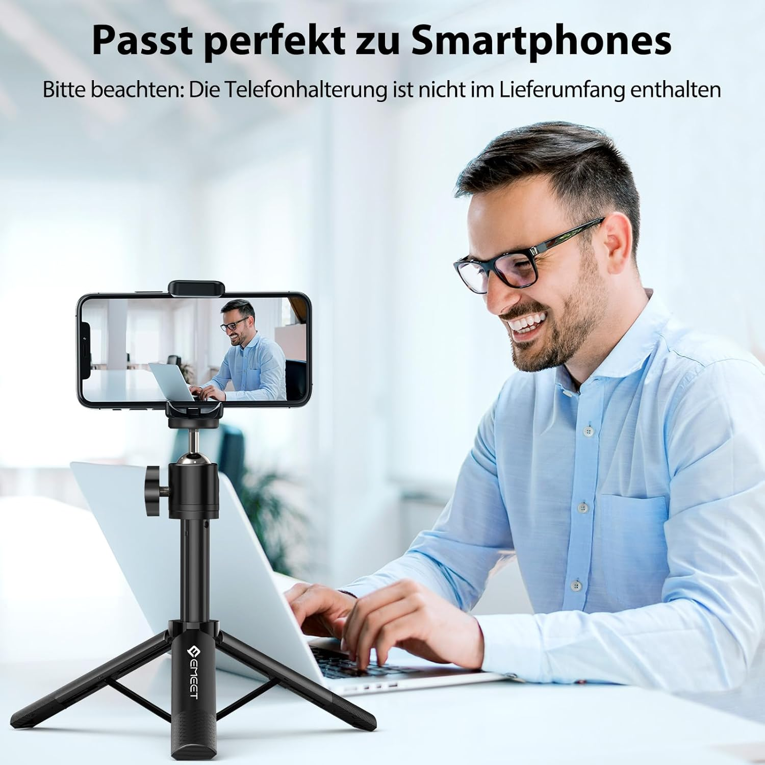 Ein lächelnder Mann nutzt einen Laptop neben einem Mini-Stativ mit Smartphone.