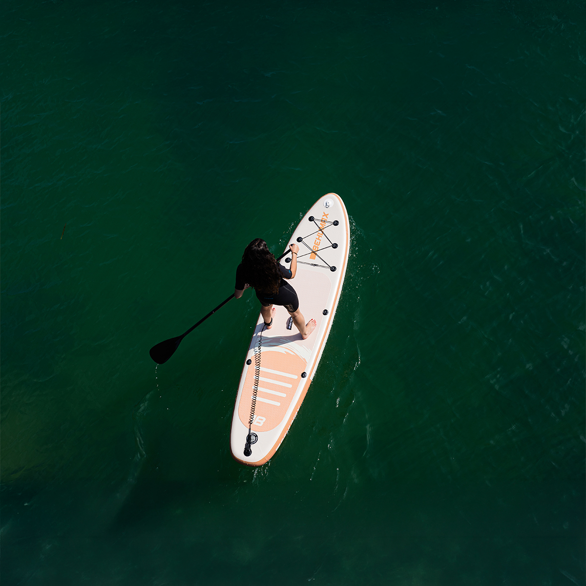 Vista aérea de una mujer haciendo pádel surf en aguas verdes y claras.