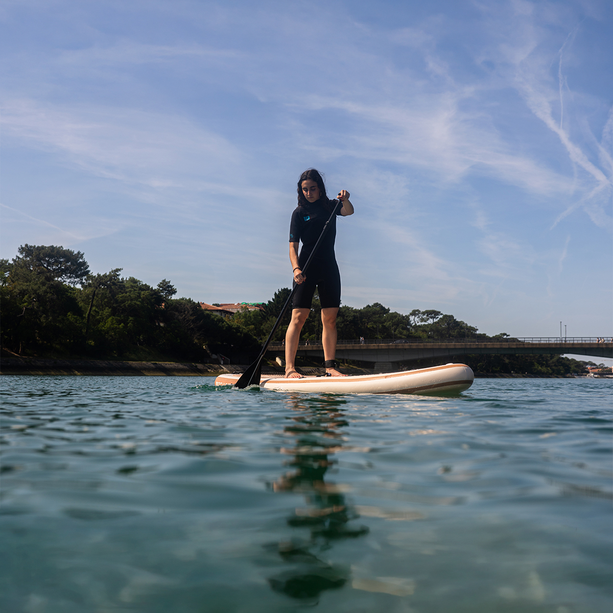 Una mujer con traje de neopreno está de pie en una tabla de surf de remo en aguas tranquilas.