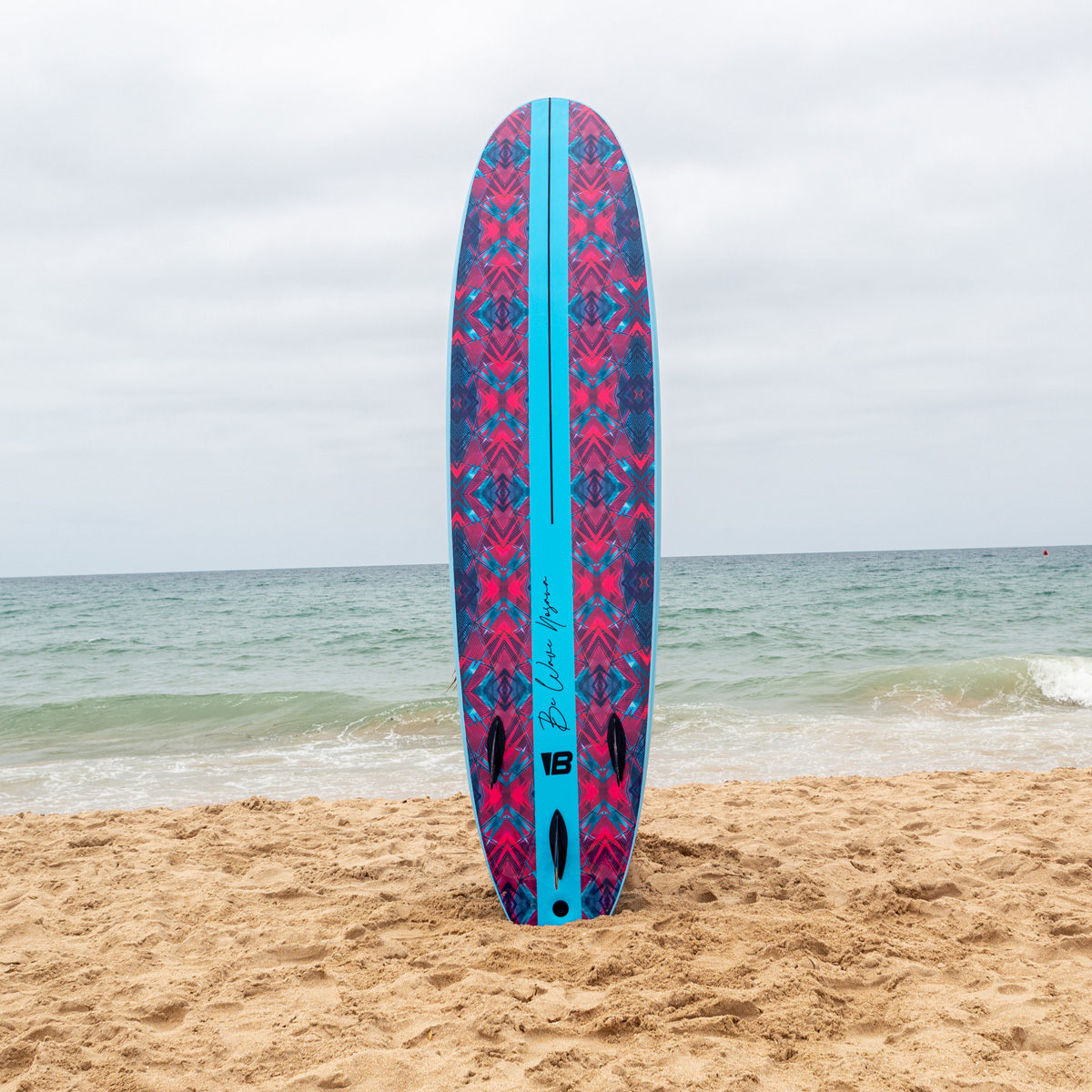 Una colorida tabla de surf con patrón rosa está de pie en la arena junto al mar.