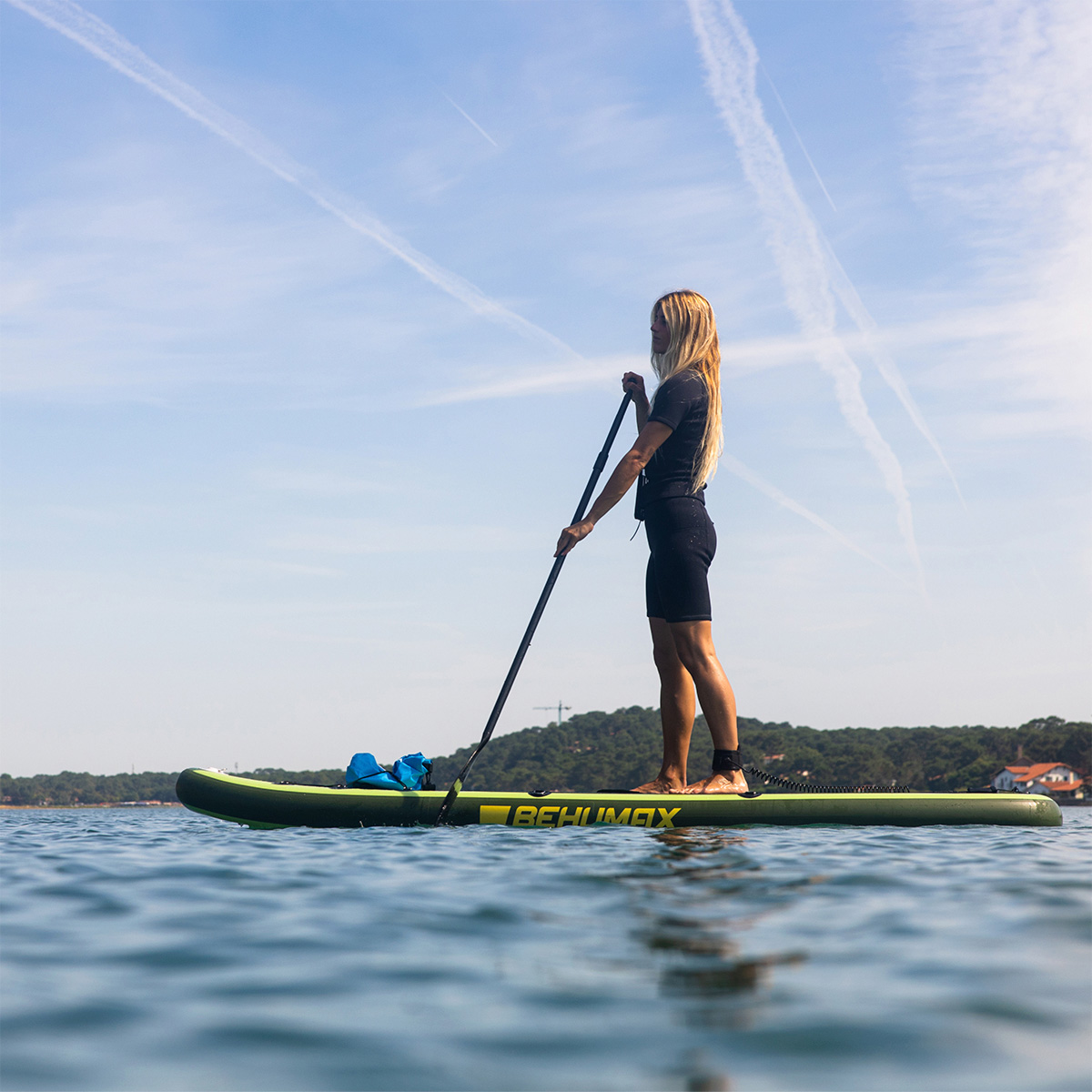 Mujer en traje de neopreno negro de pie y remando en una tabla de surf de remo verde sobre agua tranquila.