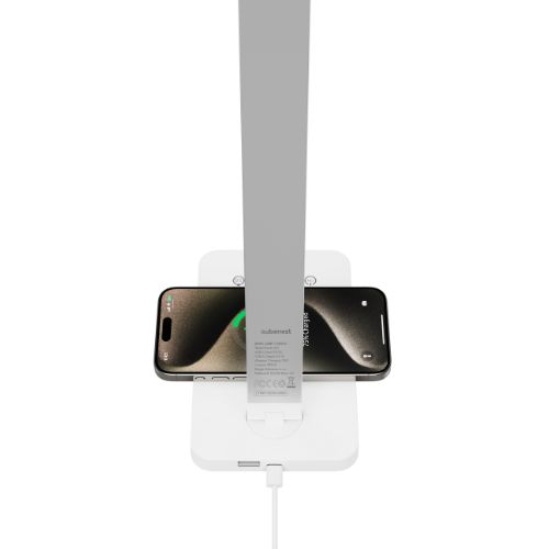 Ein schwarzes Smartphone lädt drahtlos auf einer weißen Ladestation, an der eine graue Schreibtischlampe befestigt ist.