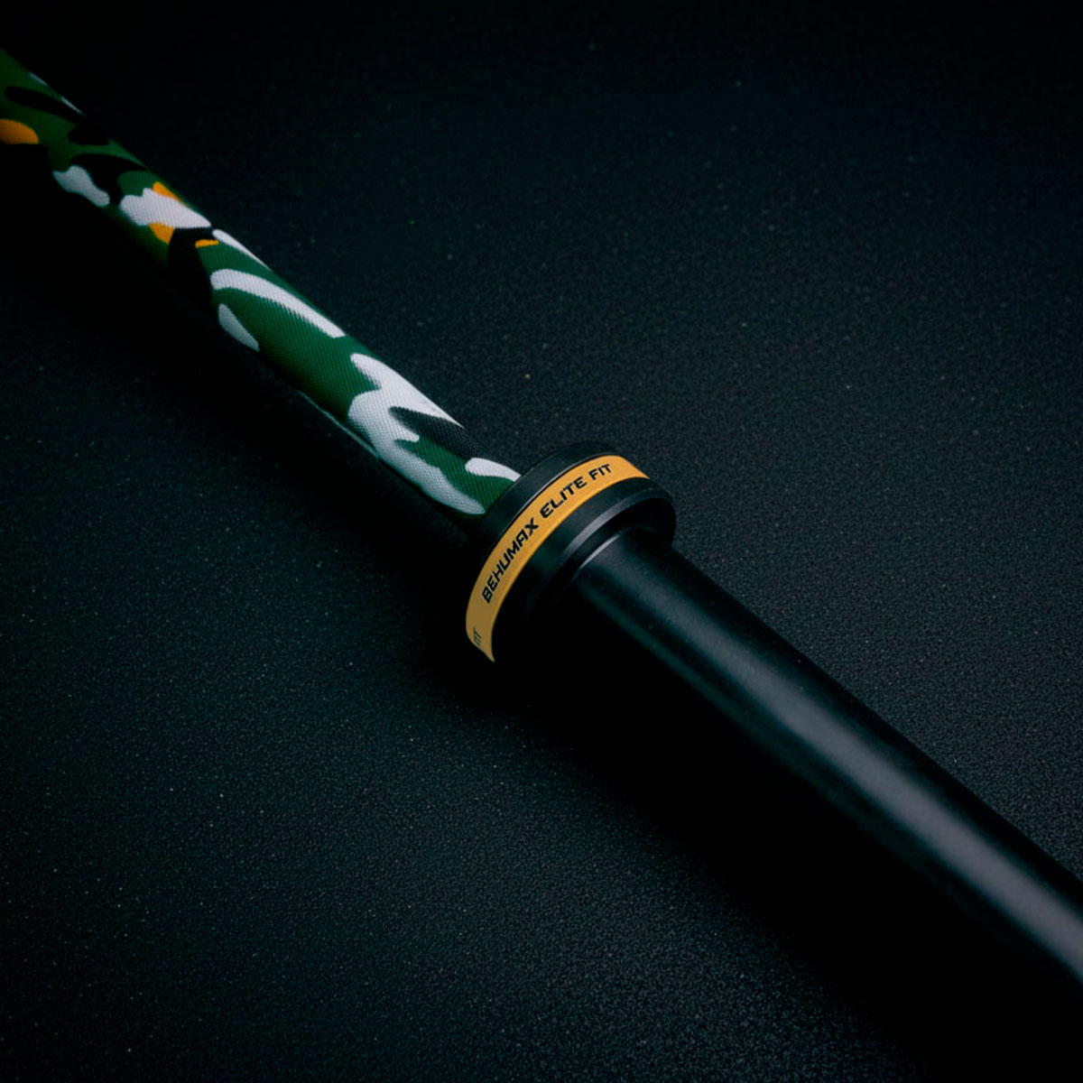 Una barra con patrón de camuflaje, mango negro y marca amarilla Behumax Elite Fit sobre fondo oscuro.