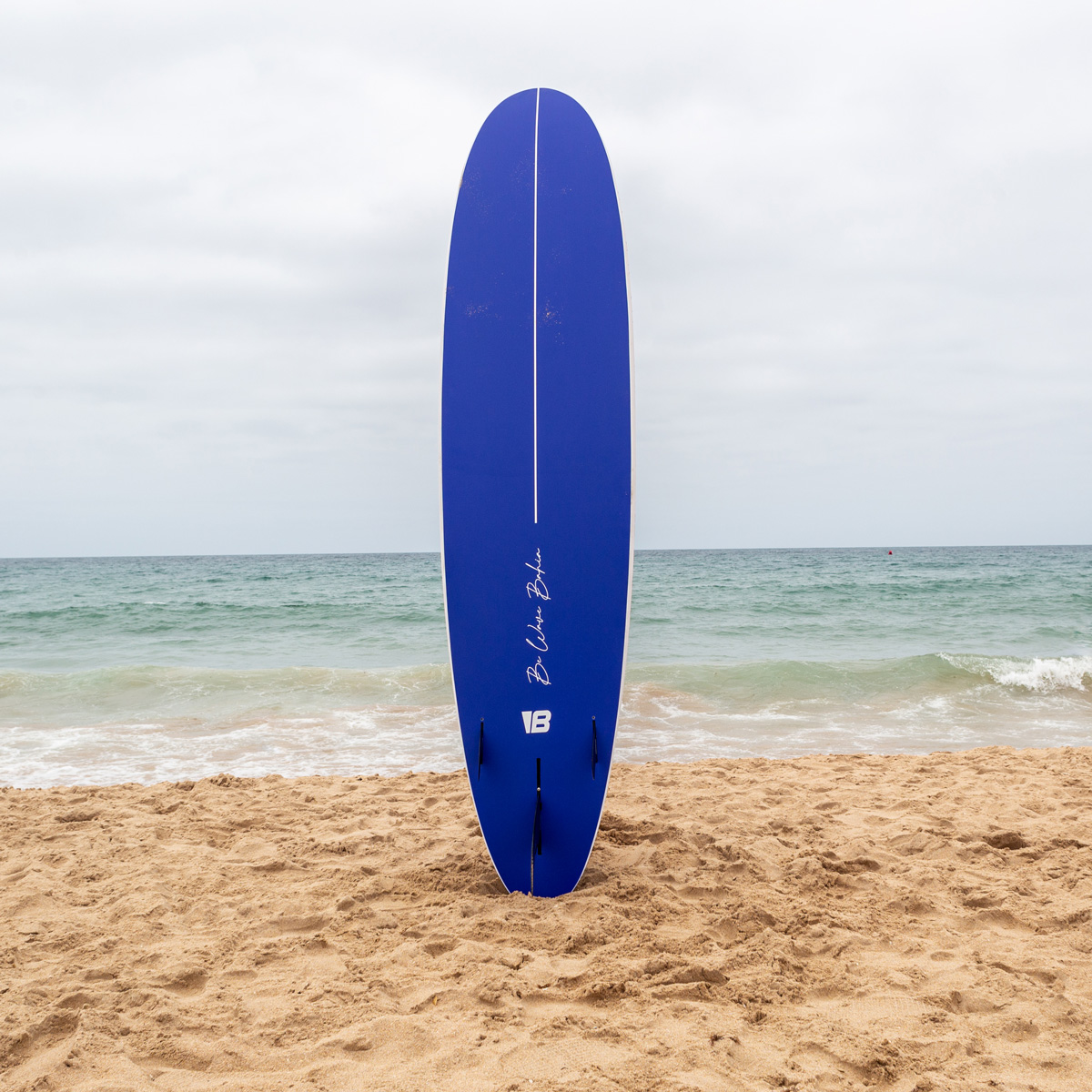 Una tabla de surf azul se encuentra erguida en la arena de una playa frente al mar.