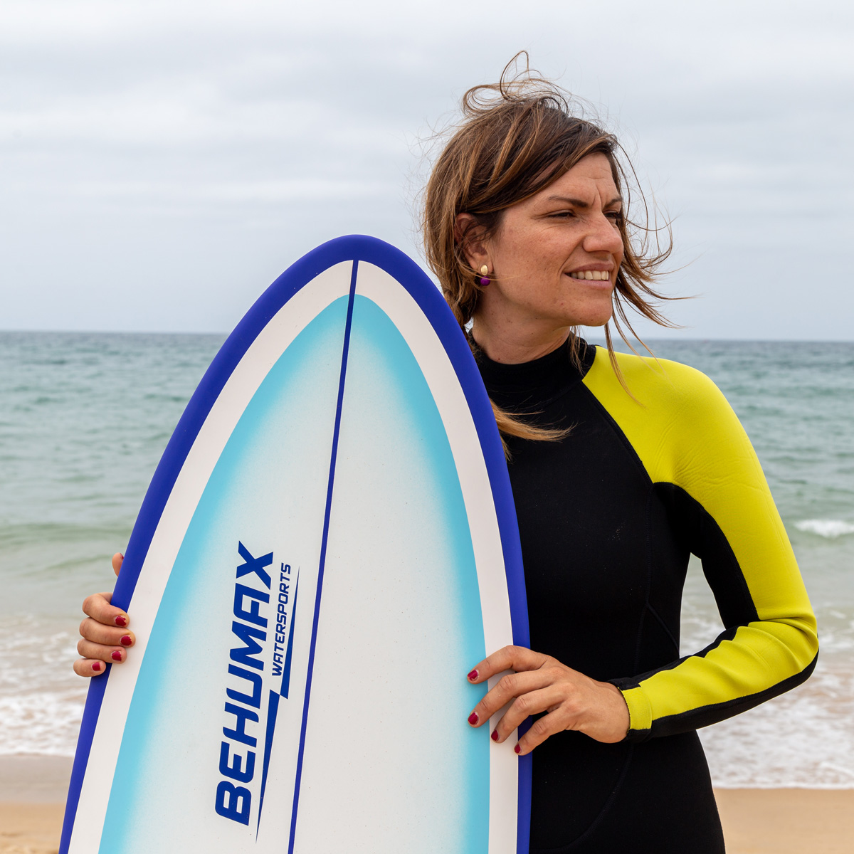 Una mujer con traje de neopreno sosteniendo una tabla de surf en la playa.