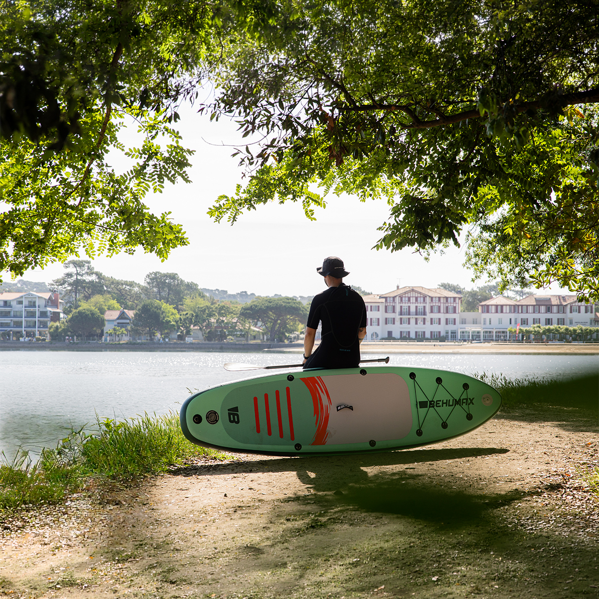 Persona sentado en una tabla de SUP junto al lago bajo árboles.