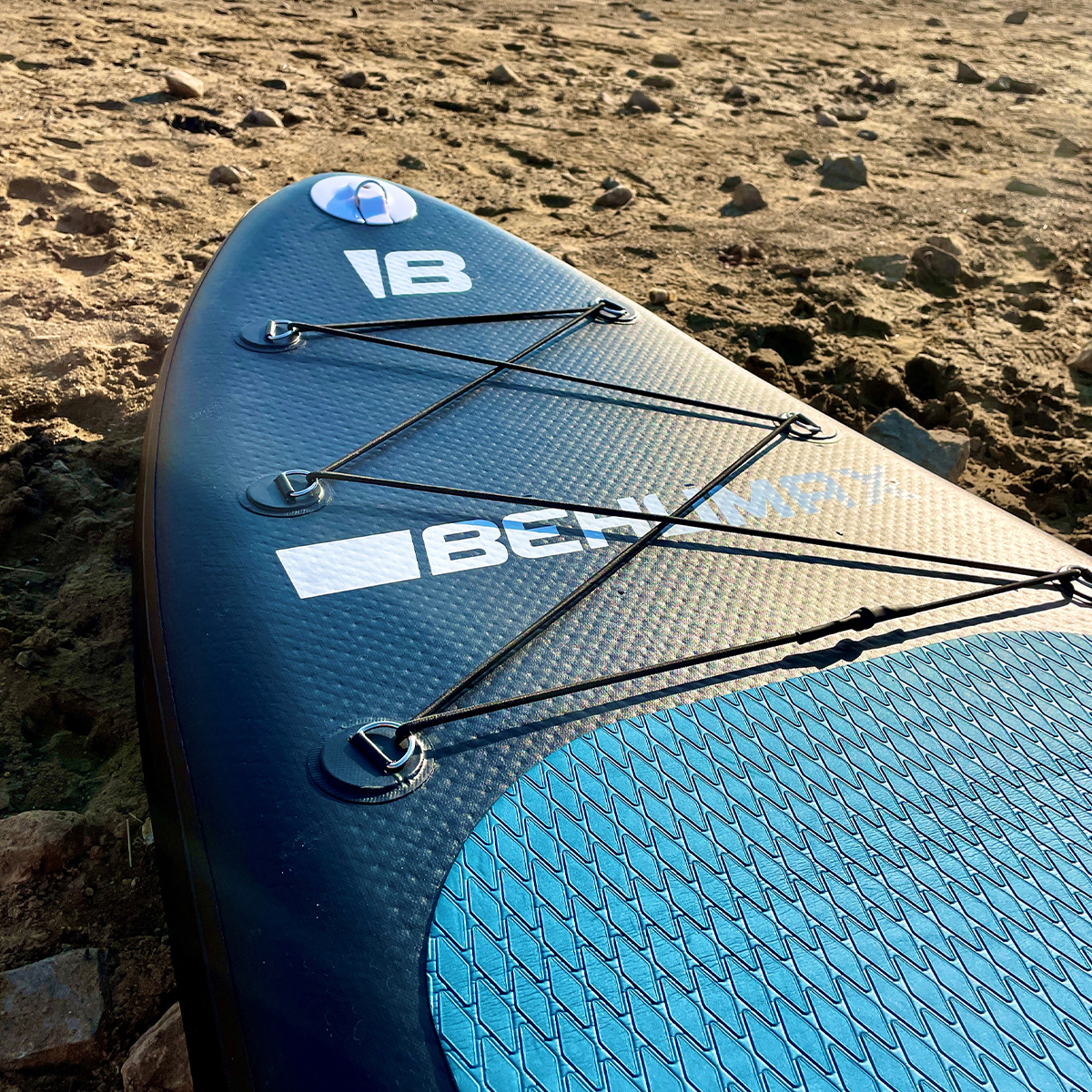 Una tabla de paddle surf azul y negra descansa en la orilla arenosa.