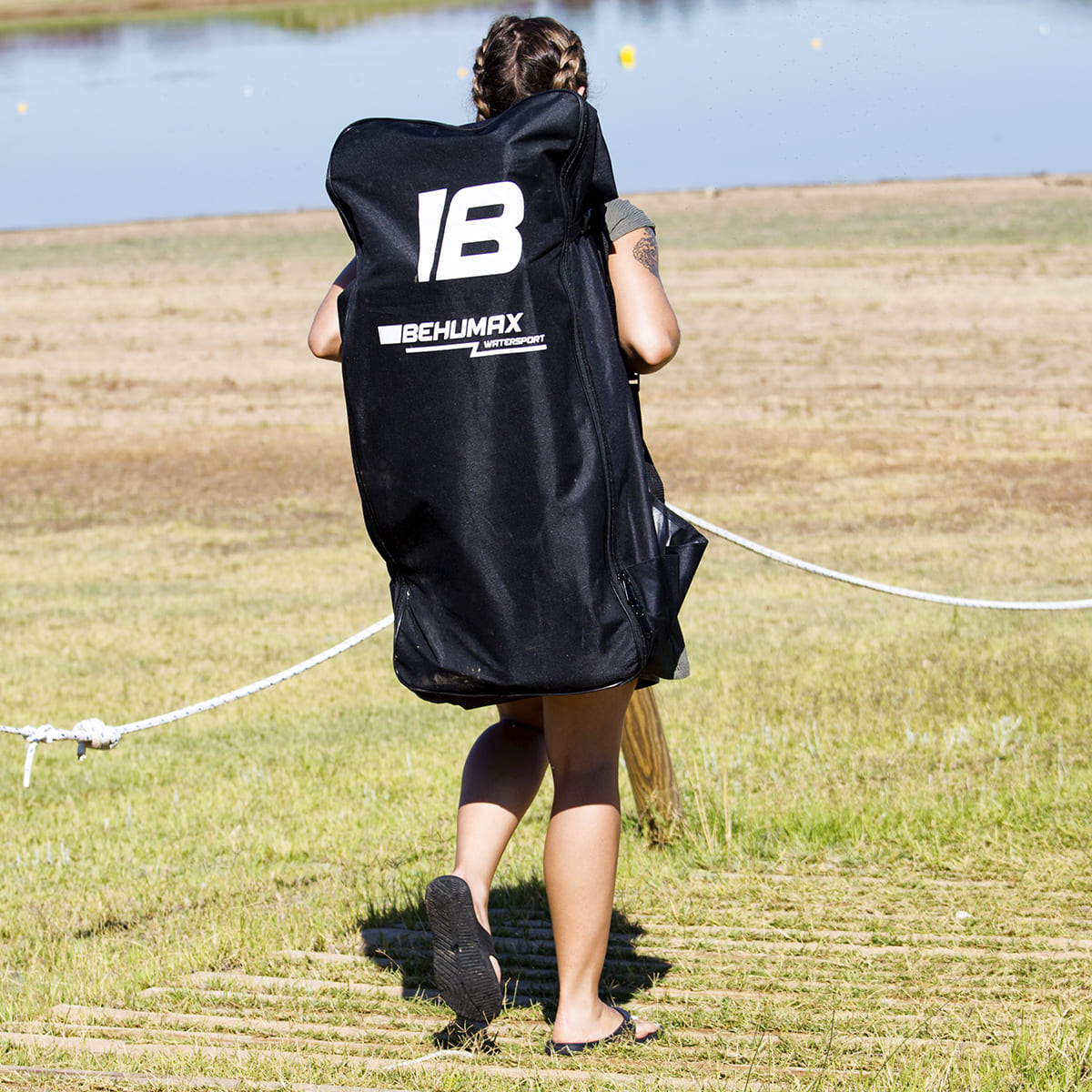 Una mujer lleva una bolsa grande y negra de Behumax watersport en la espalda al aire libre junto a un lago.