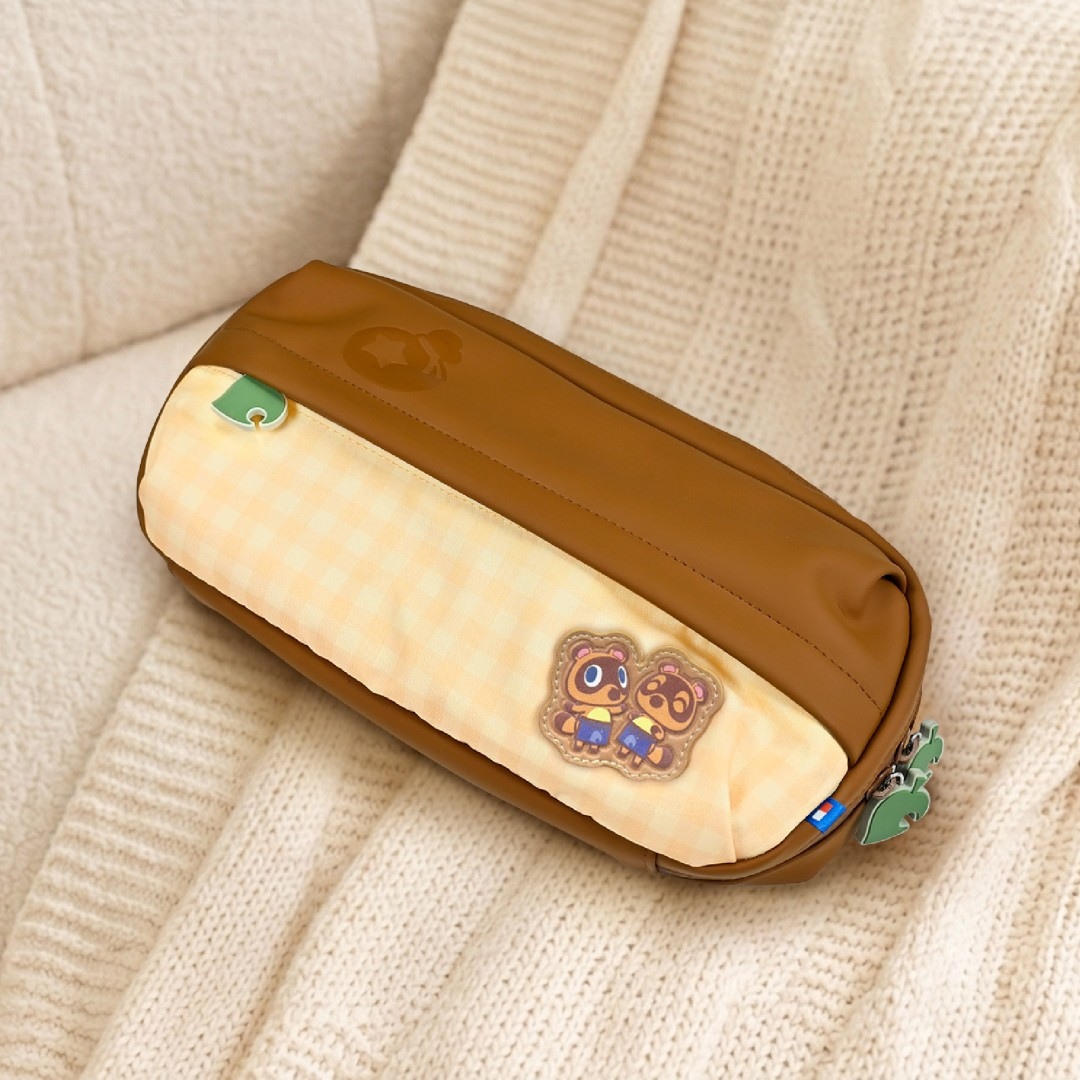 Un estuche marrón y amarillo a cuadros con mapaches de Animal Crossing descansa sobre una manta tejida.
