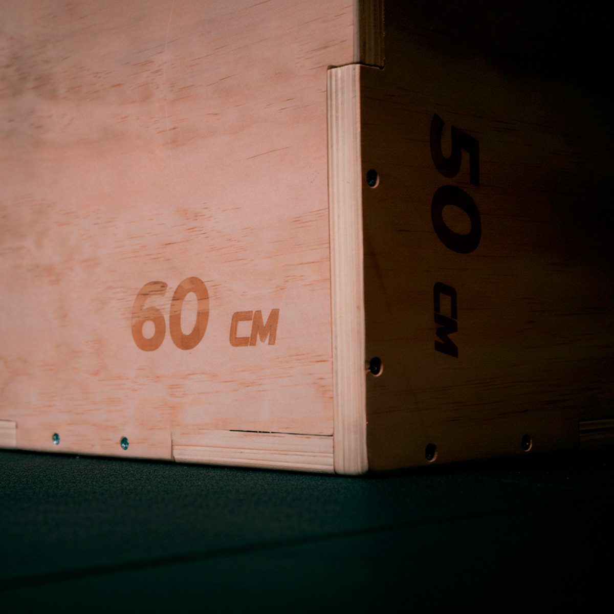 Caja pliométrica de madera con las etiquetas 60 cm y 50 cm en un suelo oscuro.