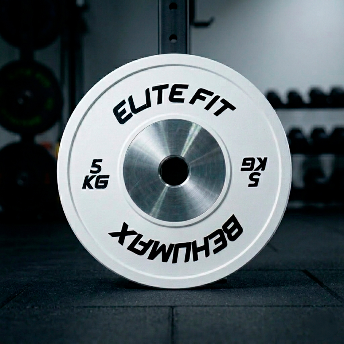 Un disco de pesas Elite Fit blanco de 5 kg está de pie en el suelo del gimnasio.