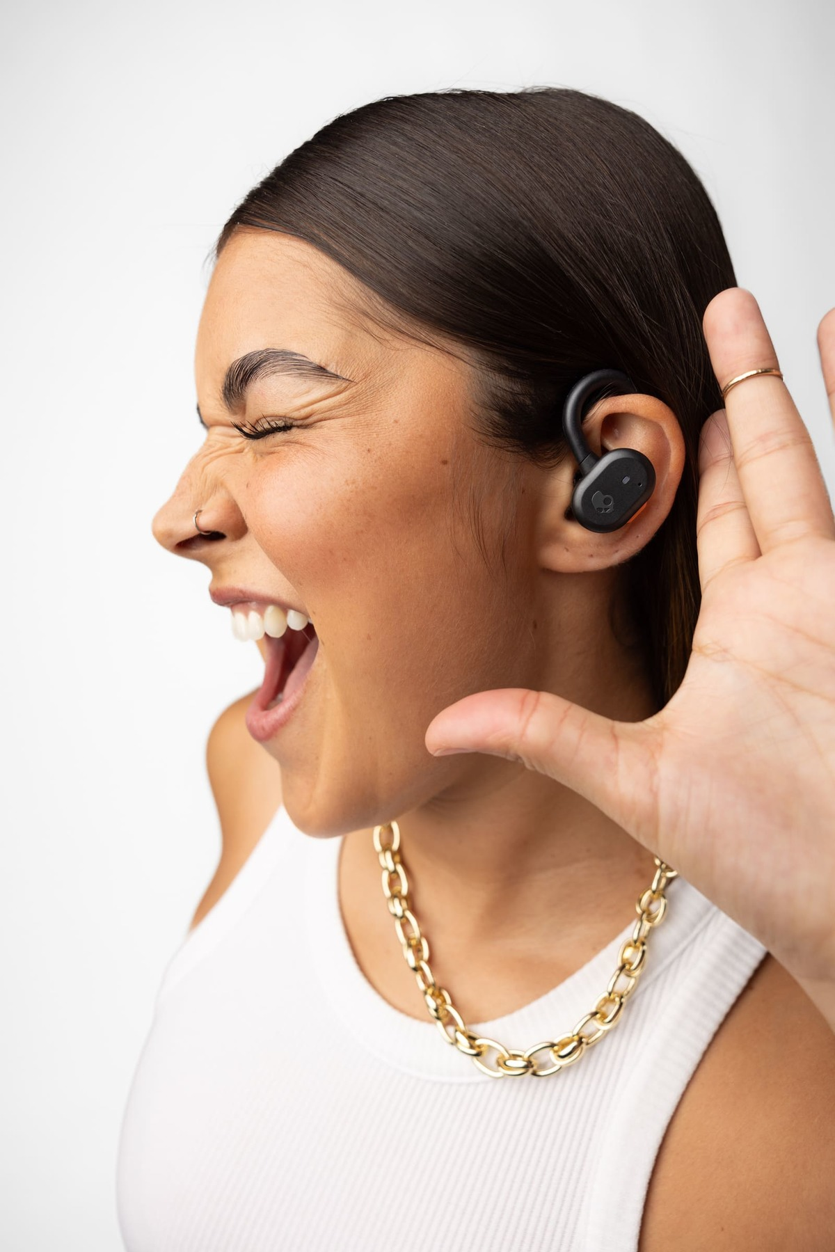 Una donna con auricolare nero e catena d'oro esulta con gli occhi chiusi e la bocca aperta.