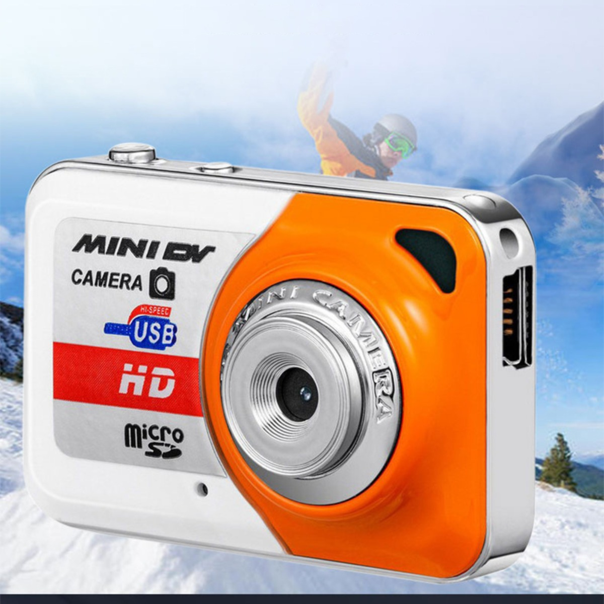 Eine weiß-orangefarbene Mini-DV-Kamera vor einem verschneiten Bergpanorama mit einem Skifahrer.